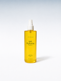 A clear plastic spray bottle filled with golden yellow body oil, featuring a white pump dispenser. The label reads 'Soft Hydrating Body oil' and 'Maya Tree Skin'.